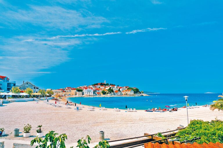 Urban beach of Primosten town with people having a rest on the background of beautiful buildings and blue sky