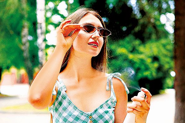Smiling woman in sunglasses spraying thermal water onto her body outdoors